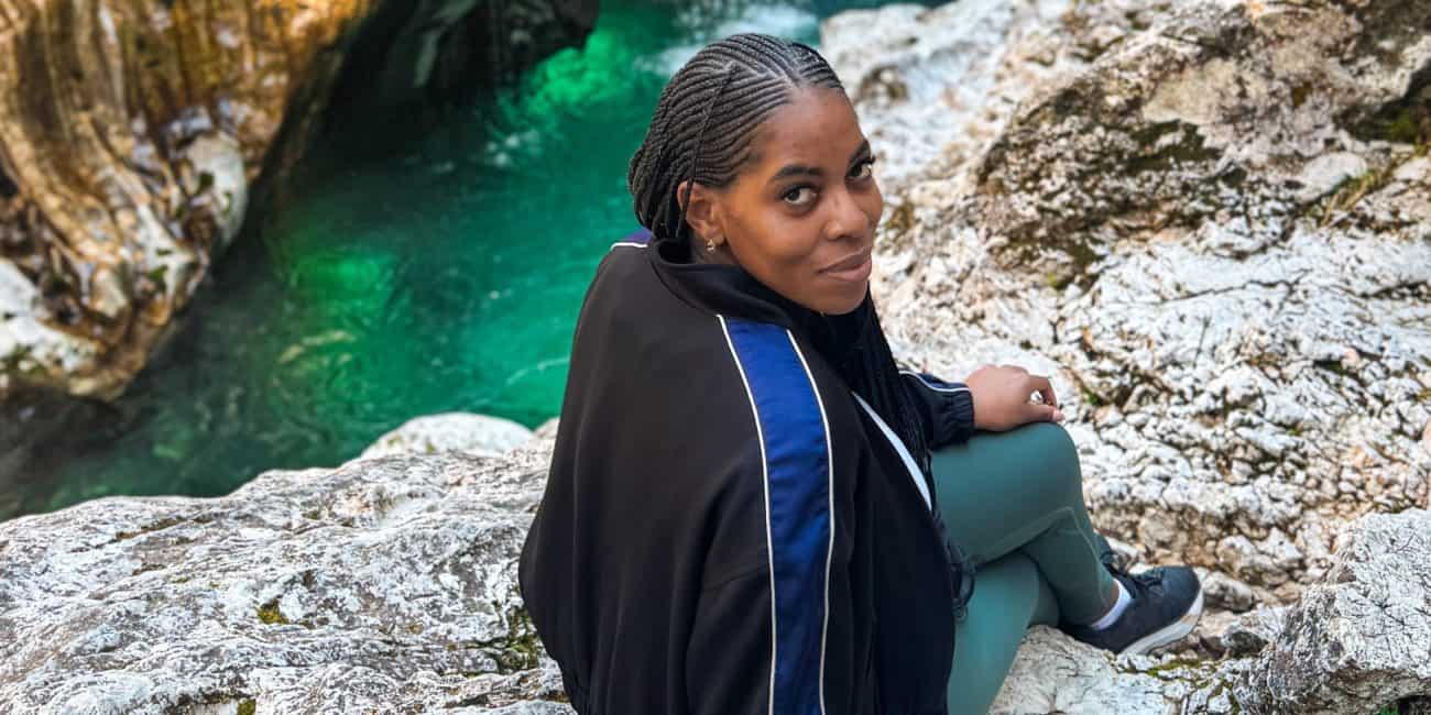 A detailed view of Nma Okafor sitting on rocks beside a scenic waterfall in Slovenia, showcasing her enjoying nature and outdoor adventure in a picturesque European landscape.