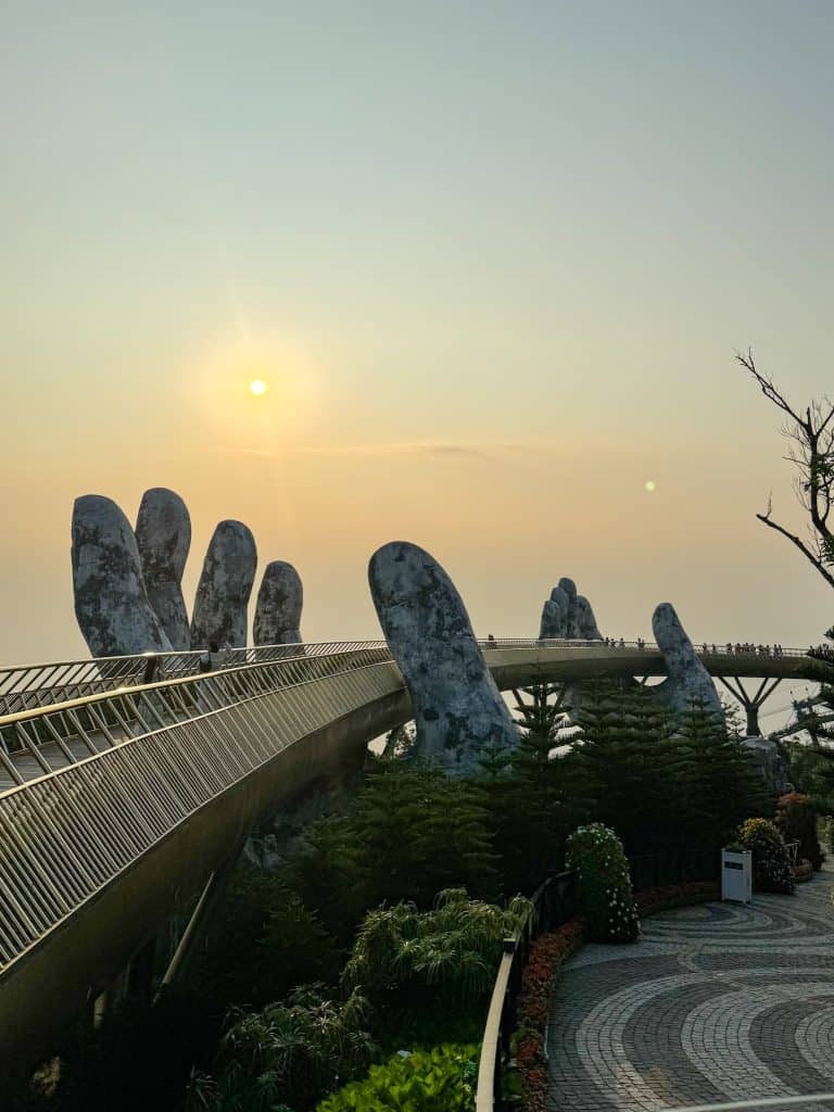 Vibrant outdoor scene featuring the stunning Golden Bridge in Vietnam, supported by giant stone hands, with lush greenery and warm sunlight creating a magical atmosphere for visitors and tourists.