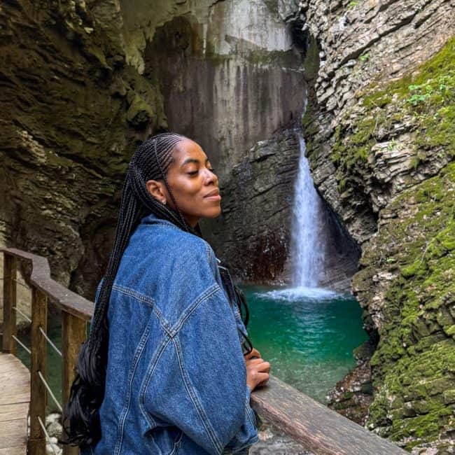 Serene woman enjoying nature at a waterfall in a lush, moss-covered canyon, showcasing outdoor adventure and travel photography.