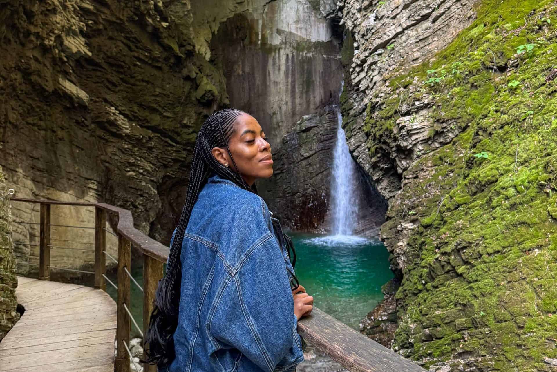 Serene woman enjoying nature at a waterfall in a lush, moss-covered canyon, showcasing outdoor adventure and travel photography.