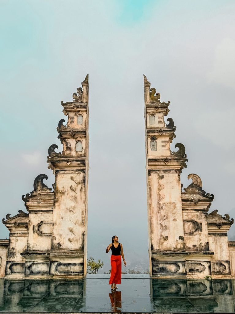 Elegant woman walking through traditional Balinese temple gate, showcasing Bali cultural architecture and tourism experience in Indonesia.