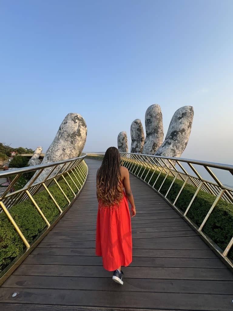 Vibrant photo of Nma Okafor walking on a scenic bridge with giant stone sculptures, showcasing her elegant style and confidence with a natural backdrop highlighting her beauty and fashion sense for SEO.