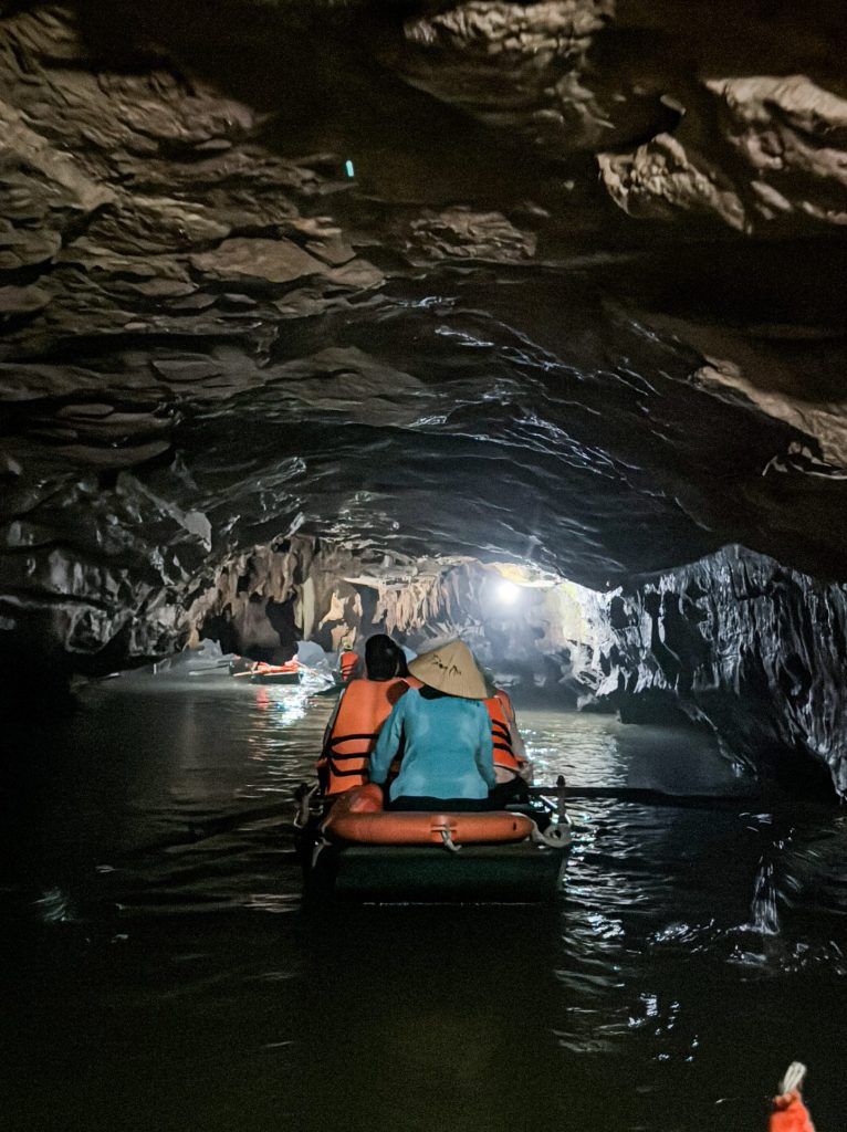 Mystery cave water adventure with visitors in a small boat exploring dark, rocky underground tunnels illuminated by a soft light.