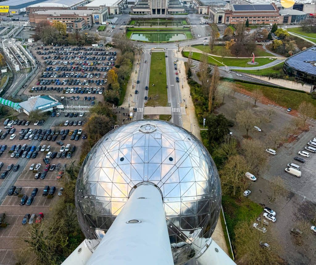 Aerial view of the Brussels from the Atomium including the iconic greenhouse dome, surrounded by parking lots, landscaped gardens, and nearby modern buildings in Brussels