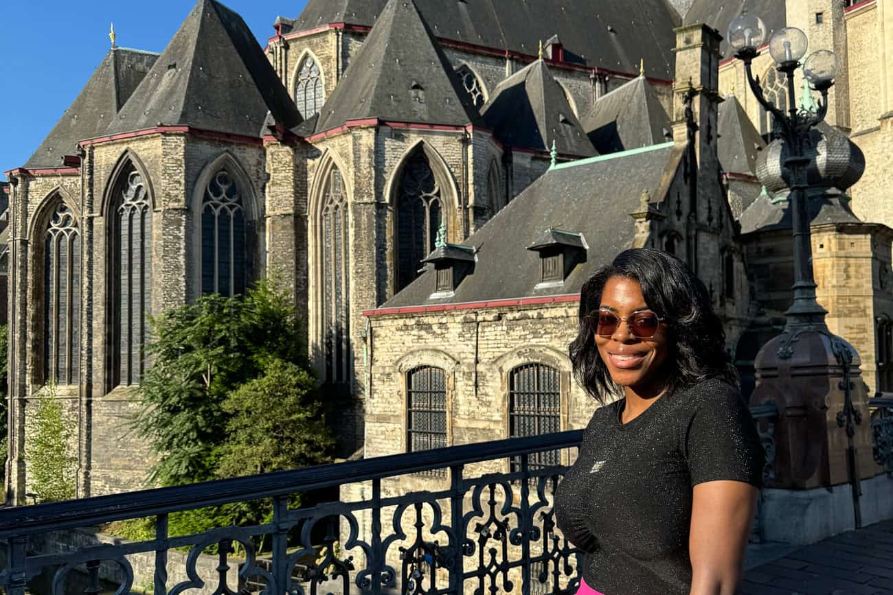 Nma Okafor smiling in front of a historic Gothic cathedral in Belgium, showcasing European architecture during her travel to top cities in Belgium.