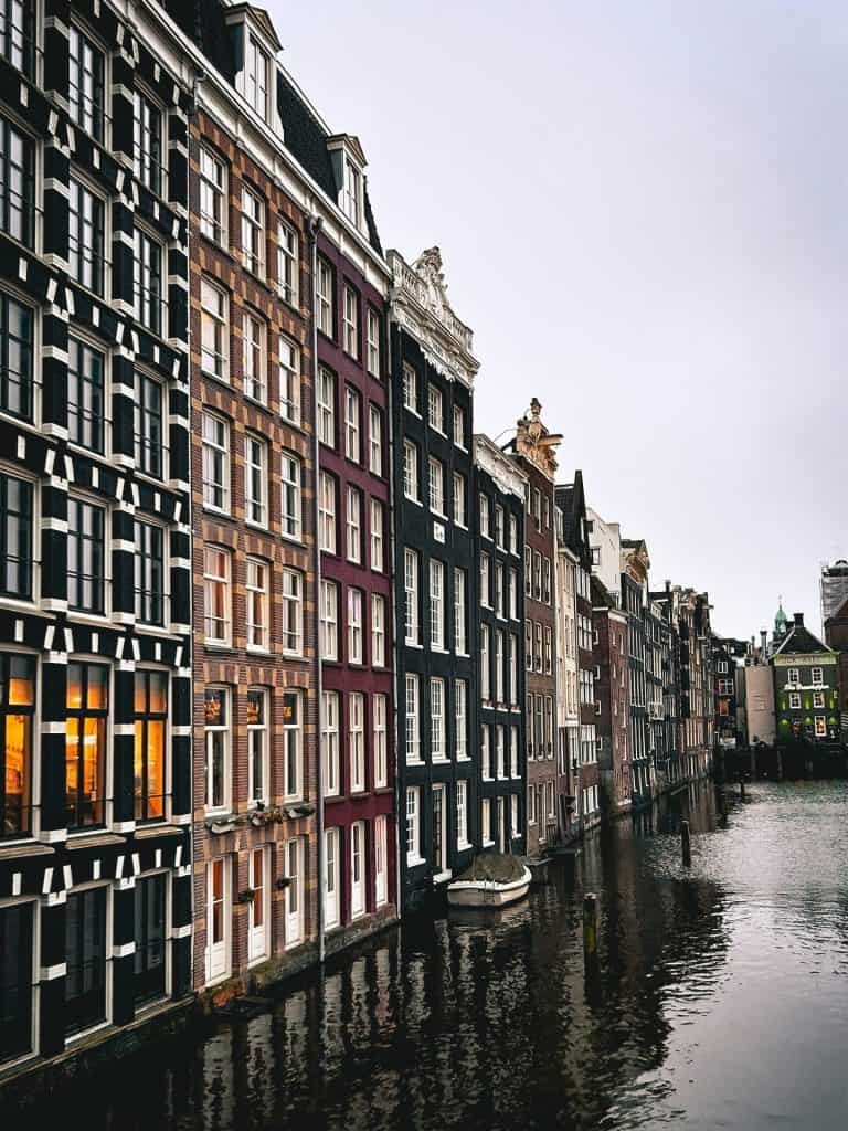 A picturesque Amsterdam canal scene in spring, featuring bicycles, boats, and vibrant greenery, perfect for experiencing tulip season in the city.