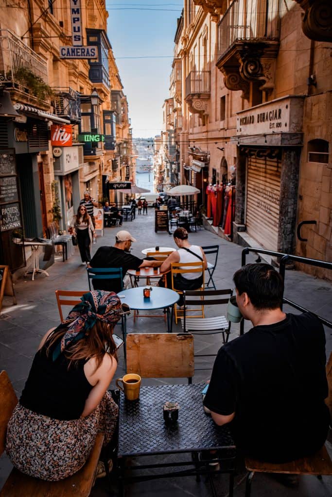 A vibrant street café scene featuring people relaxing at outdoor tables amid historic architecture and bustling city life.