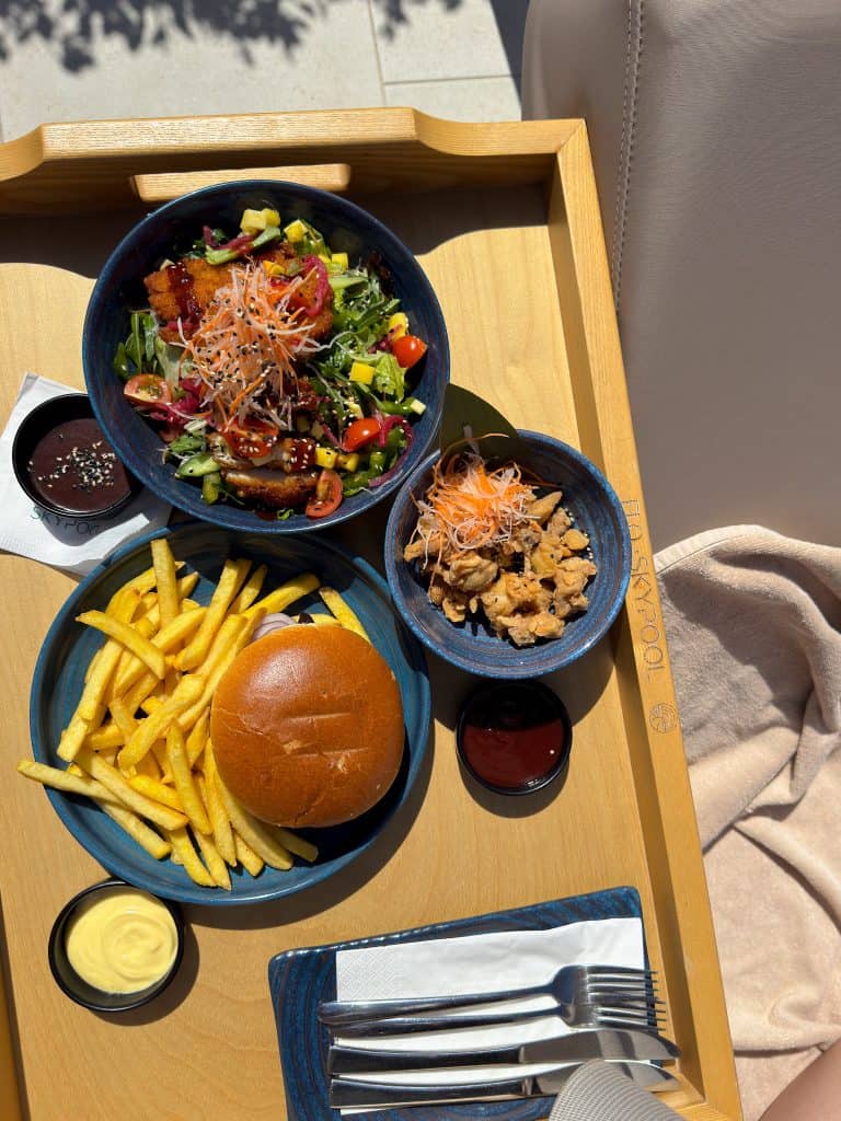 Delicious mixed salad with fresh vegetables, crispy fries, and a juicy burger served with condiments on a wooden tray. Perfect for a healthy and satisfying meal experience.