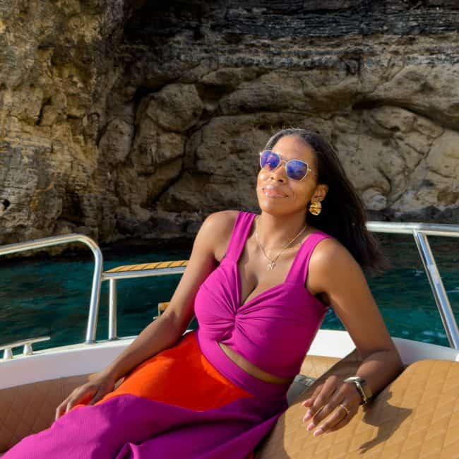 Nma Okafor relaxing on a boat in Malta, wearing sunglasses and a vibrant pink and orange dress.