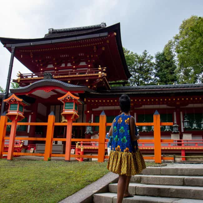 Woman in traditional Japanese kimono walking towards a Shinto shrine with red and black architecture.