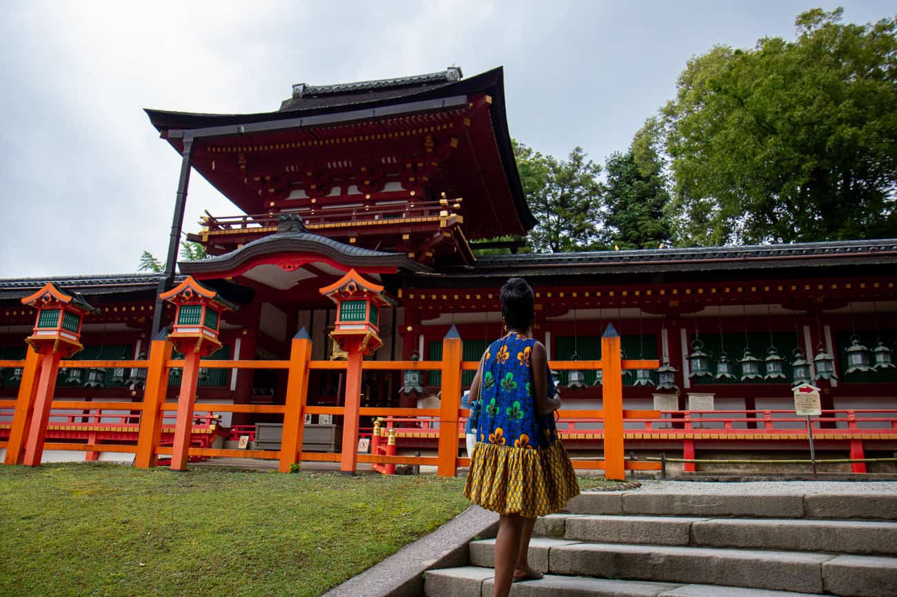 Woman in traditional Japanese kimono walking towards a Shinto shrine with red and black architecture.