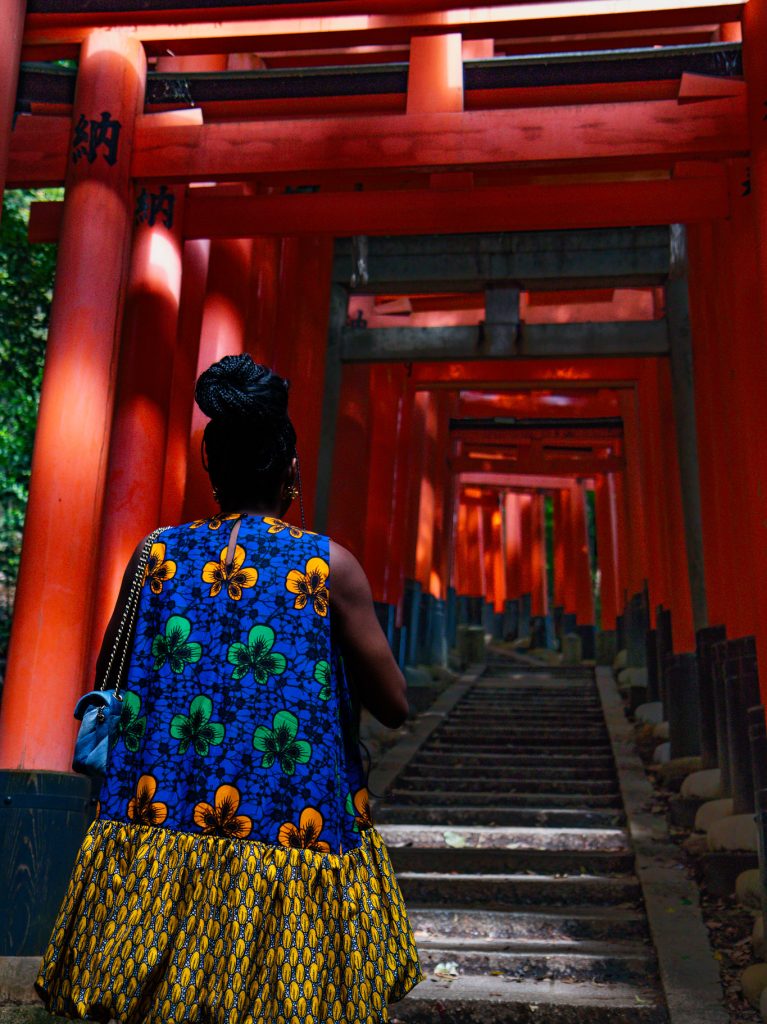 A woman in a colorful dress walking through the iconic red torii gates at Fushimi Inari Shrine in Kyoto, Japan.