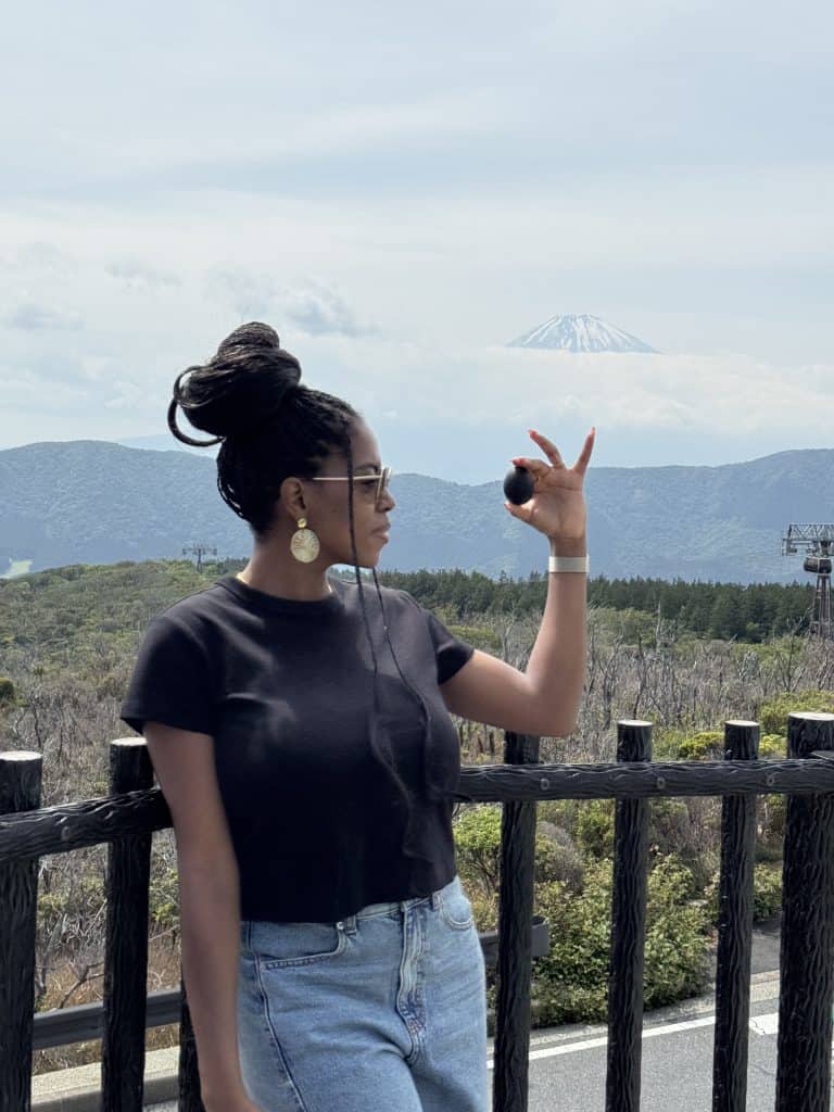 Nma Okafor standing outdoors with Mount Fuji in the background, wearing sunglasses and a black t-shirt, enjoying the scenic view during her Japan trip.
