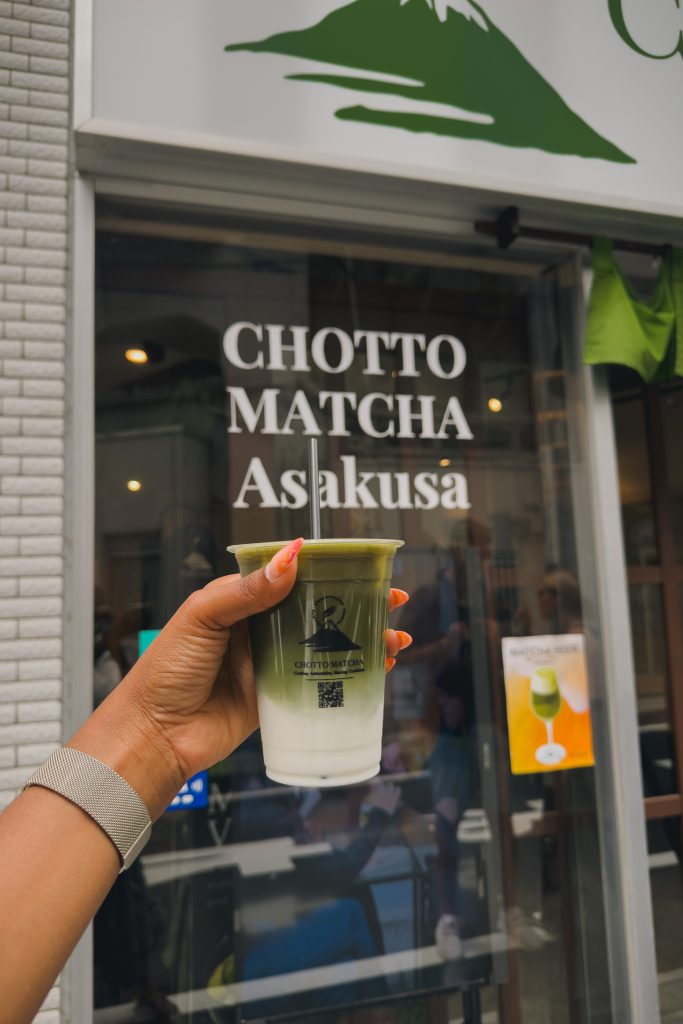 Person holding a matcha latte in front of Chotto Matte Asakusa restaurant in Tokyo, Japan.