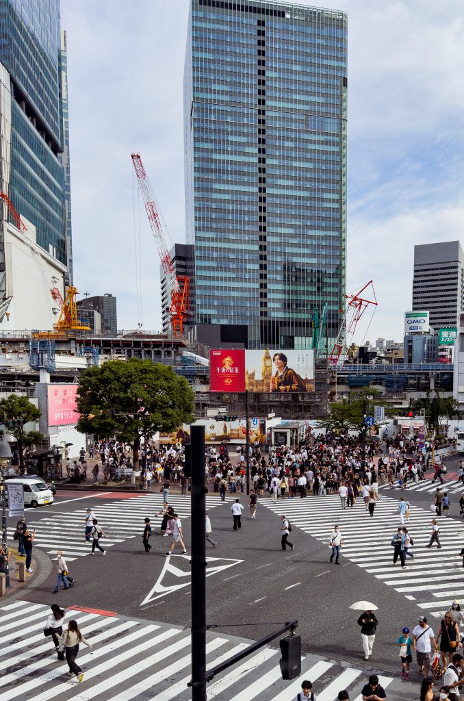Crowded Shibuya Crossing in Tokyo with pedestrians crossing in all directions and tall buildings in the background.