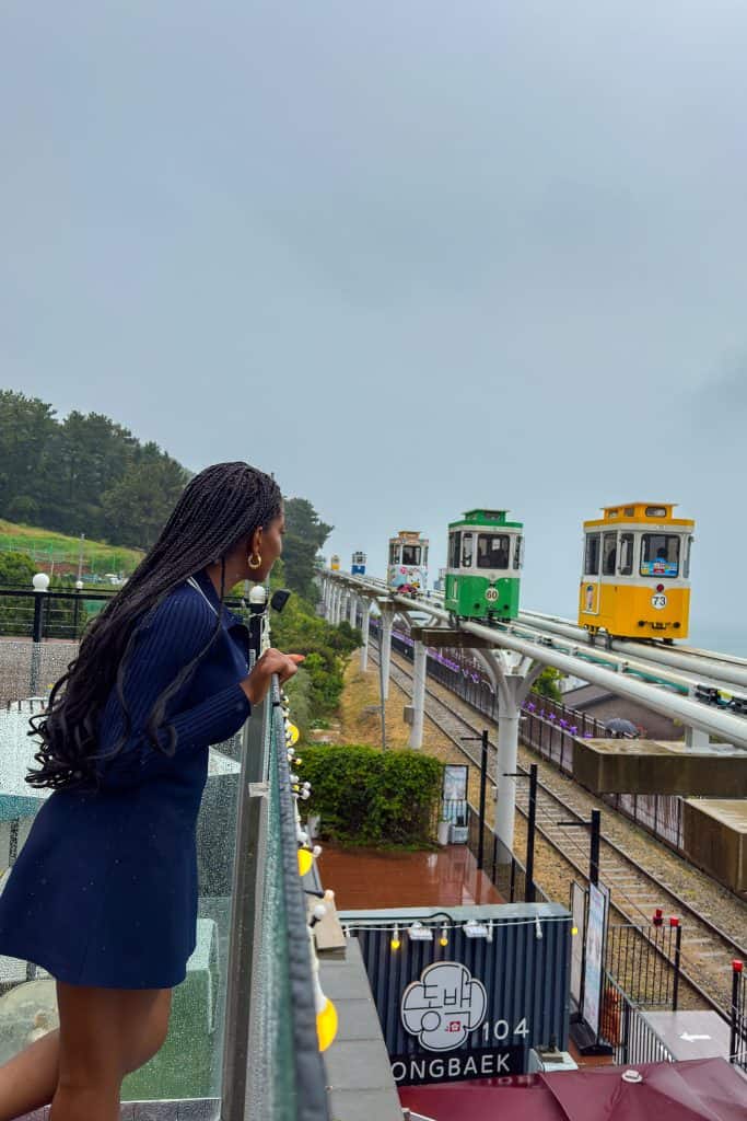 Nma Okafor enjoying the view of the Busan Sky Capsule with a train sculpture in the background during her South Korea trip.