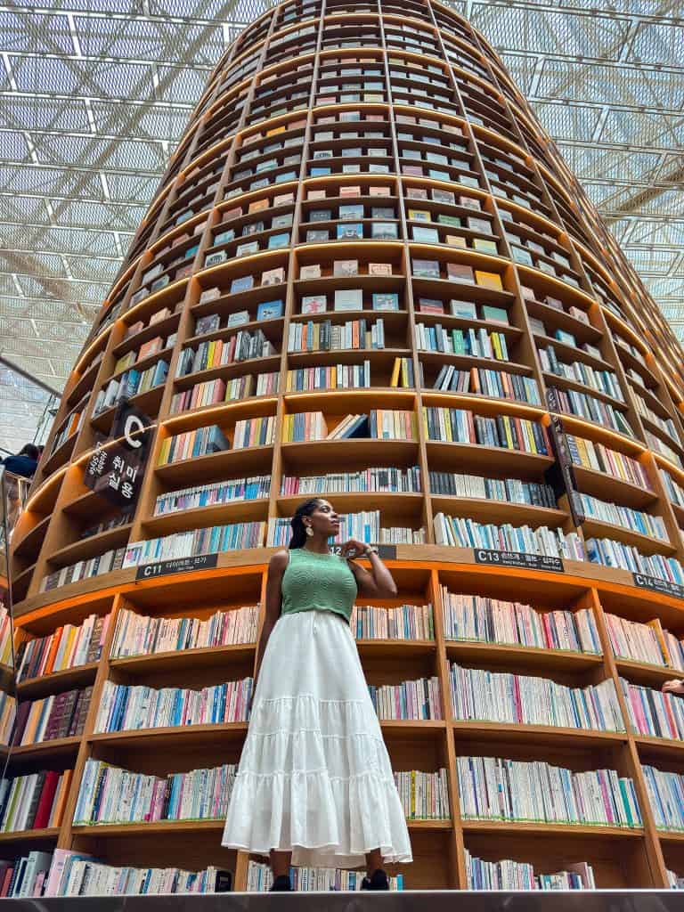 Nma Okafor standing in front of a large, curved bookshelf filled with colorful books in a modern library.