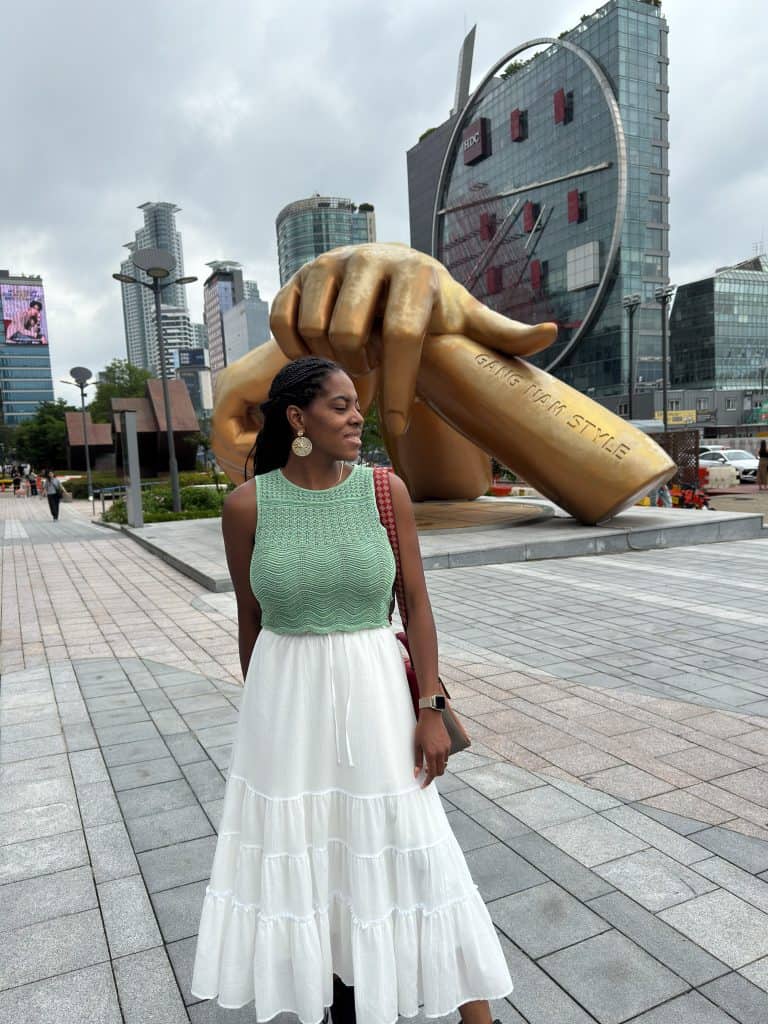 Nma Okafor standing in front of a large sculpture of a hand holding a pen in Seoul, South Korea.