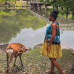 Nma Okafor standing by a serene lake in Japan, surrounded by lush greenery and traditional scenery.