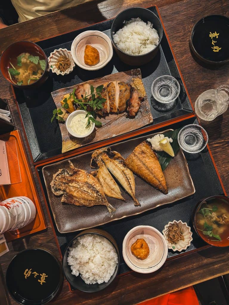 A traditional Japanese seafood meal featuring grilled fish, rice, miso soup, and side dishes served on a wooden table.