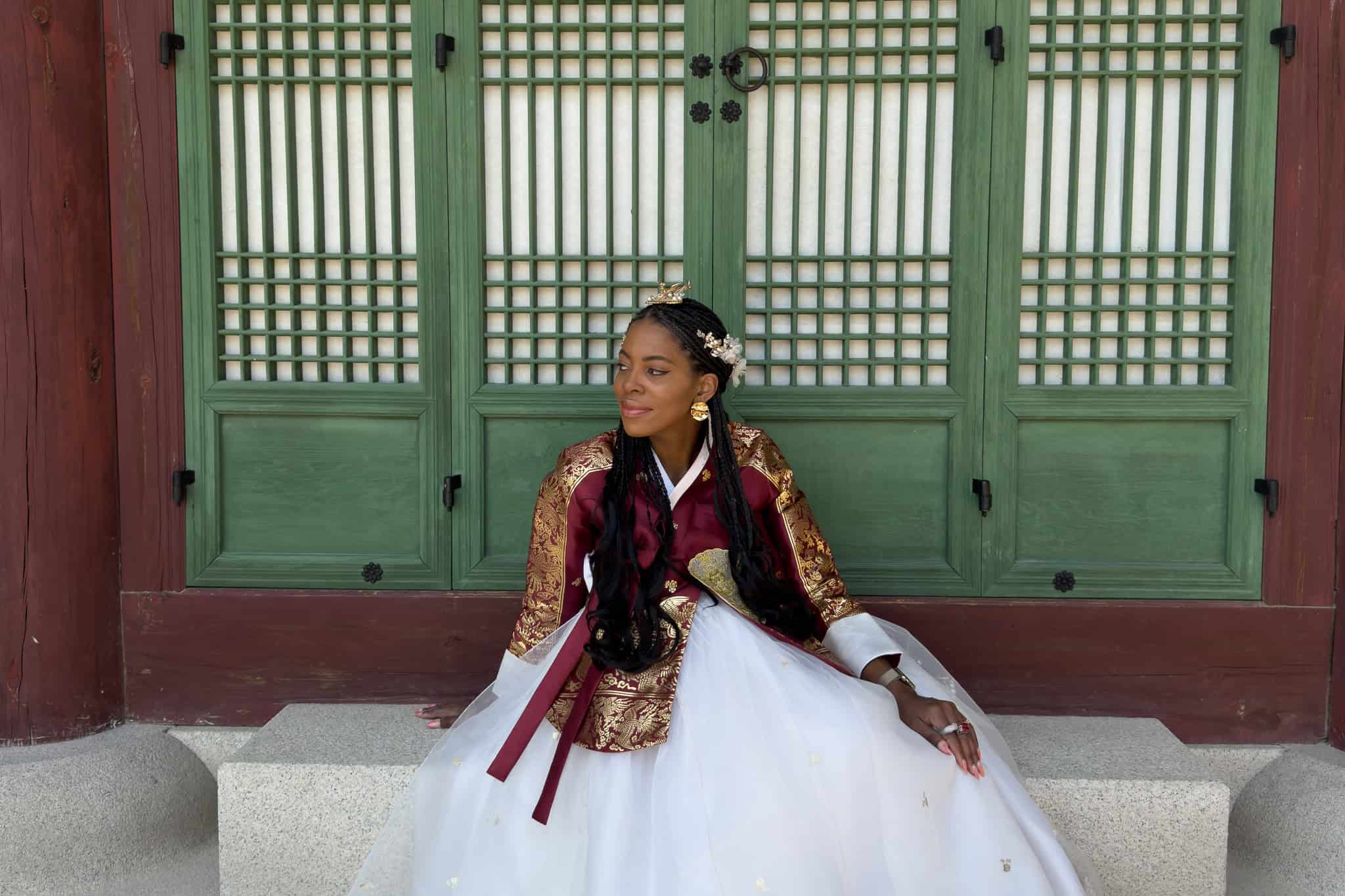 Nma Okafor dressed in traditional Korean hanbok sitting in front of a green wooden door.